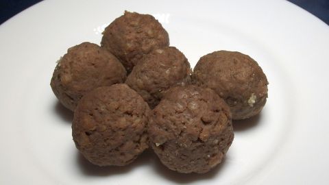 Sechs runde Leberknödel liegen appetitlich auf einem weißen Teller und warten darauf, serviert zu werden.