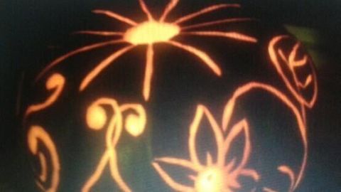 Ein geschnitzter Kürbis strahlt sanftes Licht und zeigt kunstvolle, florale Muster in einer dunklen Umgebung.