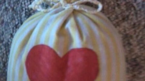 Körnerkissen-Säckchen mit einem rot gefärbten Herzmotiv, sanft auf einem grauen Teppich platziert, für Wärme und Komfort.