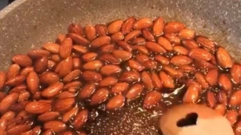 Geröstete Mandeln werden in einer Pfanne mit Sirup zubereitet, während ein Holzlöffel umgerührt wird.