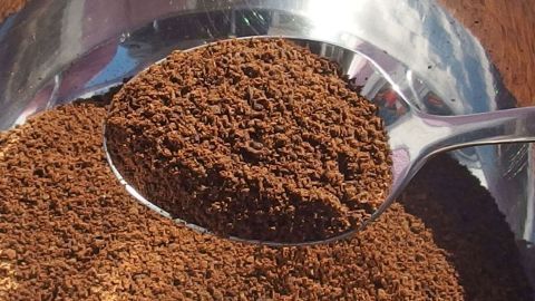 Kaffeepulver liegt in einer Schüssel, während ein Löffel das Pulver aufnimmt, um Gerüche nach dem Kochen zu neutralisieren.