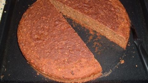 Ein großes Vollkornbrot mit Rübenkraut liegt auf einem schwarzen Blech, ein Stück wurde bereits herausgeschnitten.