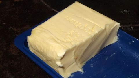 Ein Stück Butter liegt auf einem blauen Teller. Es wird verwendet, um Öl- und Fettflecke aus Kleidung zu entfernen.