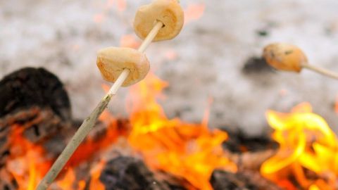 Drei Spieße mit knüppelförmigem Teig werden über einem lodernden Feuer gehalten, um Stockbrot zu rösten.