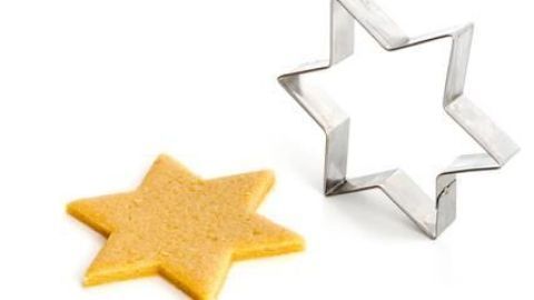 Ein Sterneausstecher steht neben einem frisch ausgestochenen Mürbeteigstern auf weißem Hintergrund.