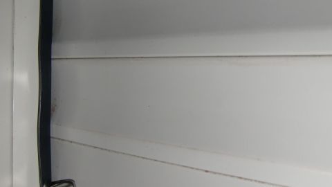 Der klappernde Rollladen bewegt sich unruhig bei Sturm, während er an einem Fenster in einem schlichten Raum hängt.