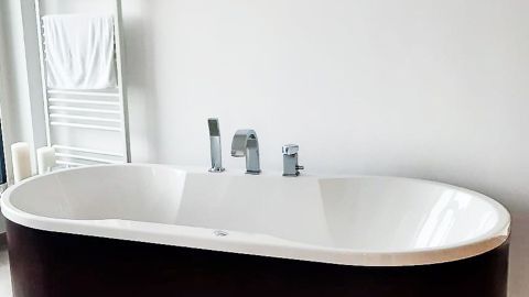 Hartnäckige Verschmutzungen in Kunststoff- oder Acrylwannen entfernen mithilfe von Orangensaft. Eine elegante Badewanne aus Acryl steht in einem modernen Badezimmer, umgeben von hellen Wänden und minimalistischer Einrichtung.