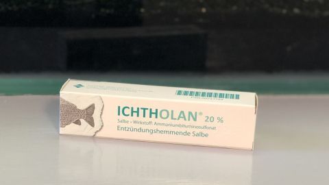 Ein Produkt mit der Aufschrift "ICHTHOLAN 20%" liegt auf einem Tisch vor einer grünen Pflanzenkulisse, ideal zur Schmerzlinderung.