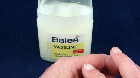 Ein Glas Balea Vaseline steht auf einem dunkelblauen Untergrund, während eine Hand es sanft berührt, um raue Haut zu behandeln.