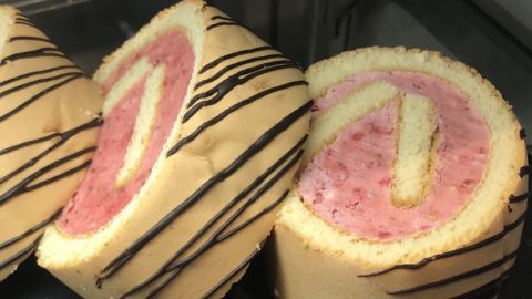 Eine Biskuitrolle liegt auf einer Fläche, dekoriert mit Schokolade, die rosa Füllung ist sichtbar und verführerisch.