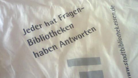 Eine Stofftasche liegt auf einem Tisch. Sie trägt den Text, der auf Bibliotheken und deren Antworten hinweist.