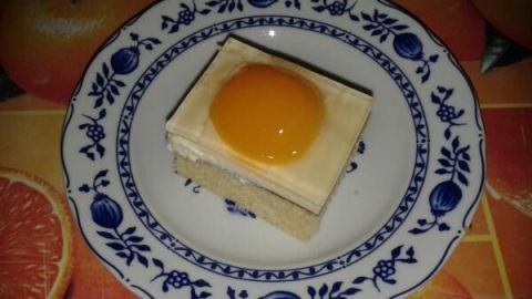 Ein Stück Spiegeleikuchen liegt dekorativ auf einem weißen Teller mit blauem Muster auf einem Tisch mit Orangenmuster.