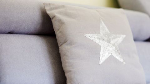 Ein grauer Kissenbezug aus einem alten T-Shirt mit einem weißen Sternmuster ruht auf einem angeordneten Sofa.