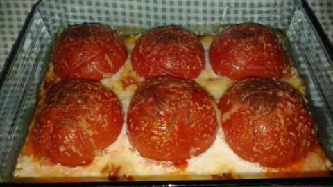 Sechs gefüllte Tomaten stehen in einer Auflaufform, umgeben von einer goldbraunen Schicht, die beim Backen entstanden ist.