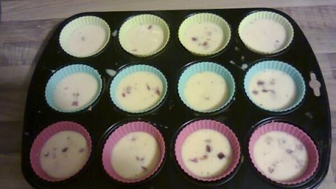 In einer Muffinform befinden sich zwölf bunte Förmchen mit einer Eimischung, die gerade vorbereitet wird.