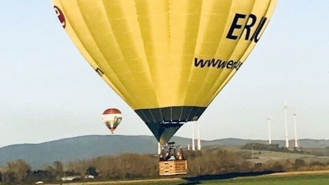 Ein gelber Heißluftballon schwebt sanft über eine grüne Wiese, während der klare Himmel im Hintergrund strahlt.