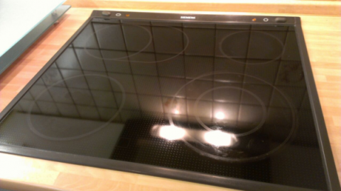 Ein glänzendes Glaskeramikfeld liegt auf einem Holzuntergrund, bereit zur Reinigung, mit gutem Licht reflektierend.