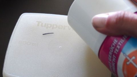 Ein Hand mit einer Sprayflasche appliziert Desinfektionsmittel gegen einen Fleck auf einem Tupperware-Behälter.