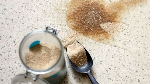 Ein Glas mit braunem Zucker steht offen auf der Küchentheke, während ein Teil des Zuckers ausgekippt ist und sich verteilt.