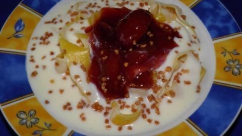 Milchnudeln liegen in einer Schüssel aus buntem Porzellan, bedeckt von Pflaumen-Rhabarber-Apfel-Grütze und dekoriert mit Samen.