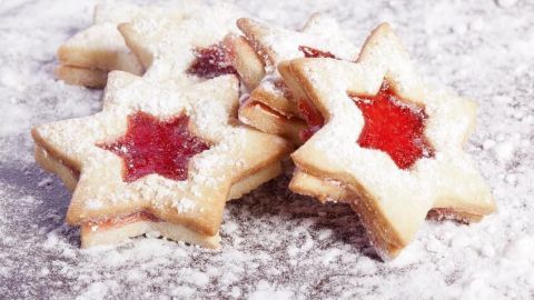 Sternförmige Spitzbuben-Plätzchen liegen auf einer glatten Oberfläche und sind mit Puderzucker bestäubt, umgeben von weihnachtlicher Stimmung.