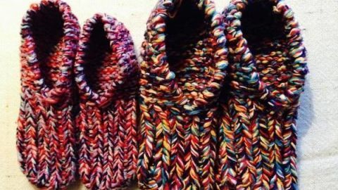 Bunte, selbstgestrickte Wollschuhe liegen auf einem hellen Untergrund, bereit zum Tragen und ideal für kalte Tage.