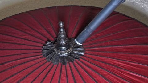 Lampenschirme verstauben recht schnell, lassen sich aber schlecht abwischen. Ein Staubsauger hilft hier weiter. Ein roter Lampenschirm wird mit einem Staubsauger entstaubt, während der Saugschlauch in die Mitte gerichtet ist.