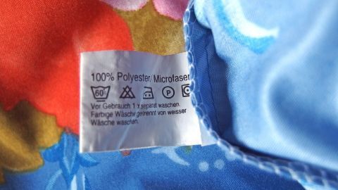 Bettwäsche aus Microfaser zeigt ein Pflegeetikett auf einem bunten, blauen Stoff mit floralen Mustern, das die Materialzusammensetzung angibt.