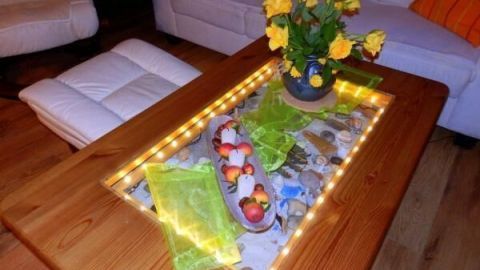 Ein Glastisch mit einer warmen Lichterkette beleuchtet, umgeben von einem gemütlichen Wohnzimmer mit gelben Blumen.