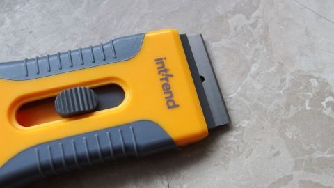Ein gelber Malermesser liegt auf einem glatten, hellen Untergrund, bereit zum Entfernen von Farbspritzern auf Fliesen.