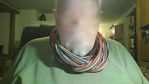 Ein Schal aus einem alten Polohemd umschließt den Hals einer Person in einem gemütlichen Raum mit Holzmöbeln.