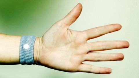 Ein Handgelenk mit einem blauen Sea-Band zur Linderung von Schwangerschaftsübelkeit ist vor einem unscharfen, grünen Hintergrund zu sehen.