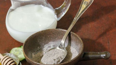 Eine Schüssel mit Heilerde und einem Löffel steht neben einer Kanne Milch, auf einem rustikalen Tisch arrangiert.