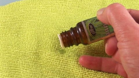Ein Hand hält eine Flasche Raumduft, während einige Tropfen auf ein grünes Tuch fallen und frischen Duft verbreiten.