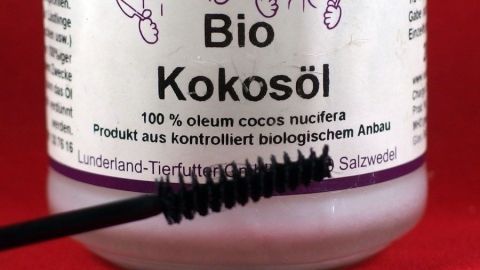 Ein Wimpernbürstchen taucht in ein Glas mit Bio-Kokosöl, um wasserfeste Wimperntusche sanft zu entfernen.