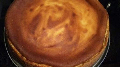 Käsekuchen sitzt frisch gebacken in einer Springform auf einem Kochfeld, seine goldene Kruste kontrastiert mit dem dunklen Herd.