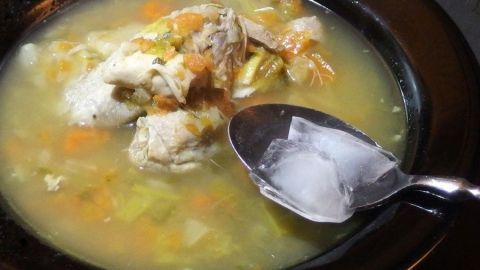 Eine Schale heiße Suppe mit einem Löffel Eiswürfeln, die zur schnellen Suppenkühlung hinzugefügt werden.