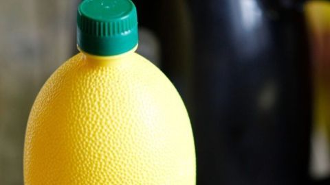 Eine gelbe Flasche mit grünem Deckel steht im Vordergrund, während ein schwarzer Wasserkocher im Hintergrund sichtbar ist.