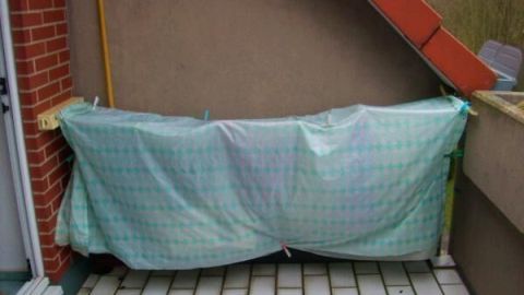 Auf einer Terrasse hängt eine Reihe Wäsche, die mit einem Tuch vor einem Schauer geschützt ist.