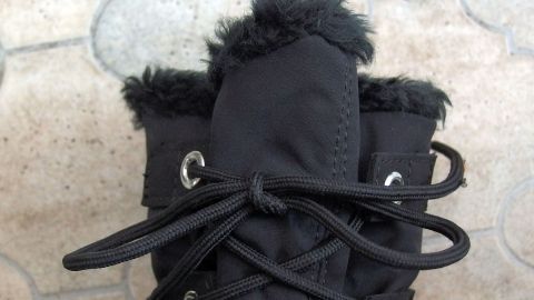Ein Paar schwarze Stiefel mit Schnürsenkeln liegt auf einem grauen, gepflasterten Boden. Die Schnürsenkel sind fest gebunden.