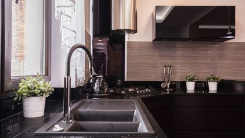 Eine Granitspüle steht auf einer dunklen Arbeitsplatte. Wasser fließt aus dem modernen Wasserhahn, während die Umgebung eine elegante Küche zeigt.
