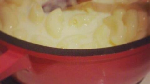Eine rote Schüssel mit Milchnudeln wird mit einem Holzlöffel verrührt, um einen cremigen Pudding zu kreieren.