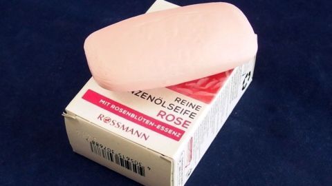 Ein rosa Seifenstück liegt auf einer weißen Verpackung mit rotem Text, umgeben von einem dunklen Hintergrund.