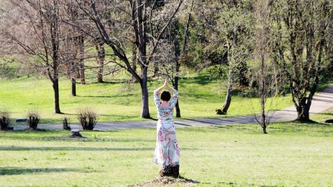 Eine Person meditiert in einem grünen Park, um Kopfschmerzen zu lindern, während Bäume und Sträucher die Umgebung prägen.