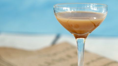 Ein elegantes Glas mit Nusslikör steht auf einem Tisch, umgeben von ganzen Nüssen und einem neutralen Hintergrund.