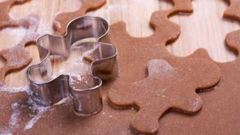 Ausstechform schneidet Lebkuchenfiguren aus braunem Teig auf bemehltem Holzbrett. Keine weiteren Details im Bild.