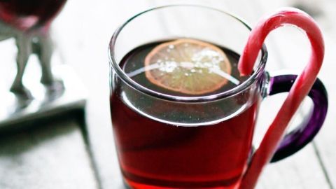 Ein Glas Früchtepunsch mit einer Zuckerstange steht neben einer kleinen Deko-Rentierfigur auf einem Holztisch.