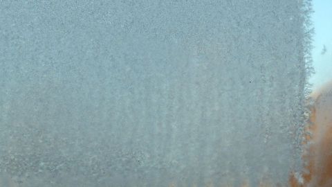 Eine vereiste Windschutzscheibe zeigt eisige Kristalle, die die Sicht beeinträchtigen, umgeben von unscharfen Hintergründen.