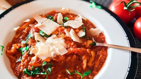 Eine Schüssel mit Pesto-Nudelschnecken in Tomatensoße, dekoriert mit Parmesan und frischen Kräutern, daneben frische Tomaten.