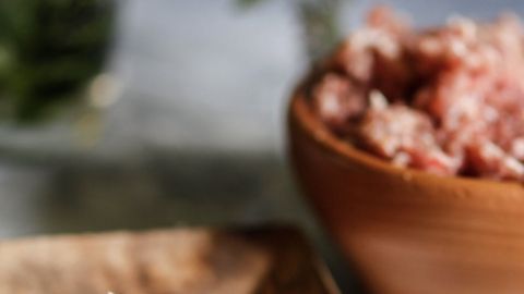 Hackbällchen liegen attraktiv auf einem Holzbrett, während eine Schüssel mit weiteren Hackbällchen im Hintergrund sichtbar ist.